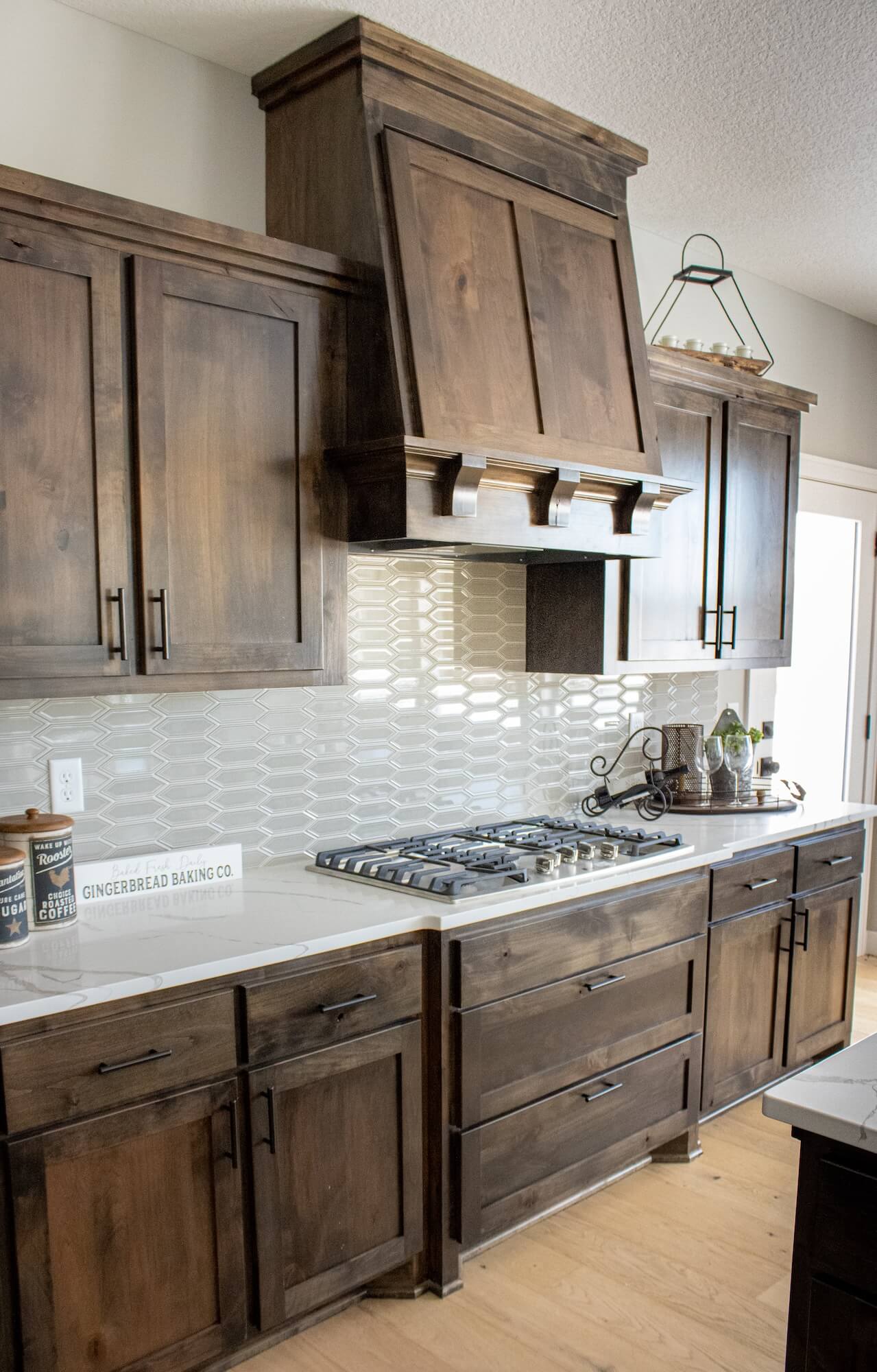 Kitchen range with dark wood cabinets, white counter tops and a patterned white backsplash.